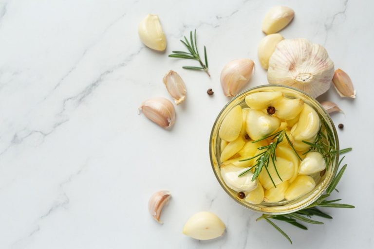Garlic cloves with rosemary in a jar on marble background.