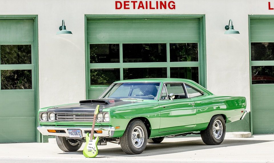 Green classic car parked with a lime guitar in front of a detailing shop.