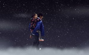 Child piggyback on snowy night wearing blue coat.