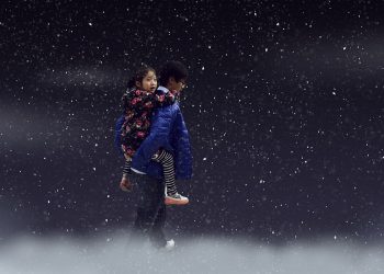 Child piggyback on snowy night wearing blue coat.