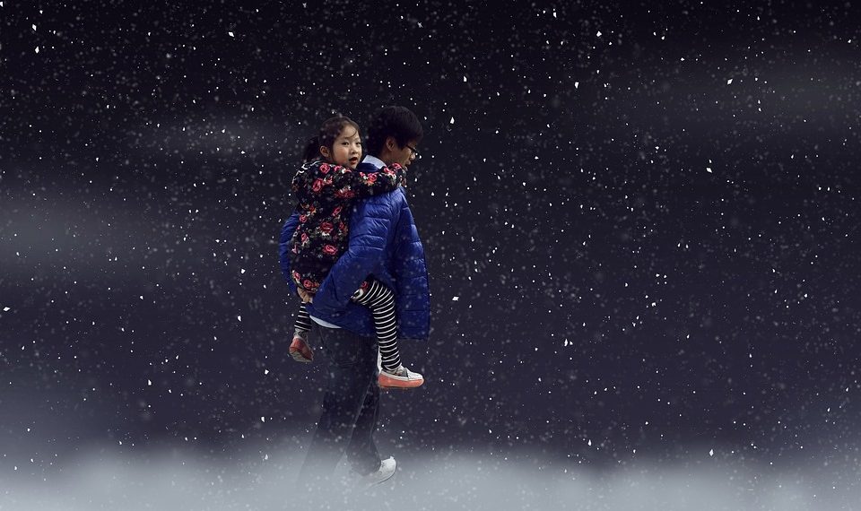 Child piggyback on snowy night wearing blue coat.