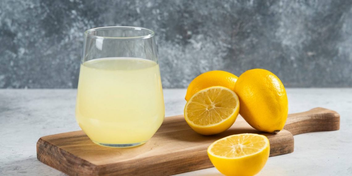 Glass of lemonade with fresh lemons on a wooden board.