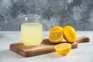 Glass of lemonade with fresh lemons on a wooden board.
