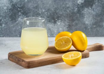 Glass of lemonade with fresh lemons on a wooden board.