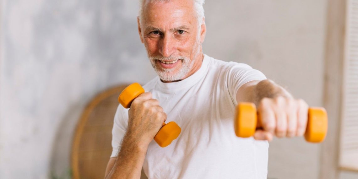 Senior man exercising with dumbbells indoors.