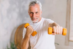 Senior man exercising with dumbbells indoors.
