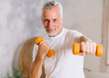 Senior man exercising with dumbbells indoors.