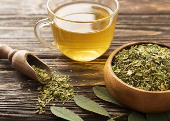 Cup of moringa tea next to dried moringa leaves in a wooden bowl.