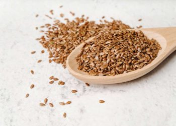 Wooden spoon filled with flaxseeds on a marble surface.