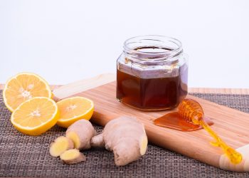 Lemon slices and ginger with a jar of honey on a wooden board.