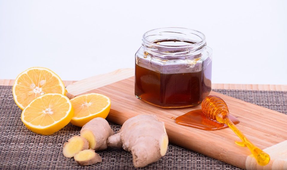 Lemon slices and ginger with a jar of honey on a wooden board.