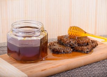 Honey jar and honeycomb on wooden board with dipper.