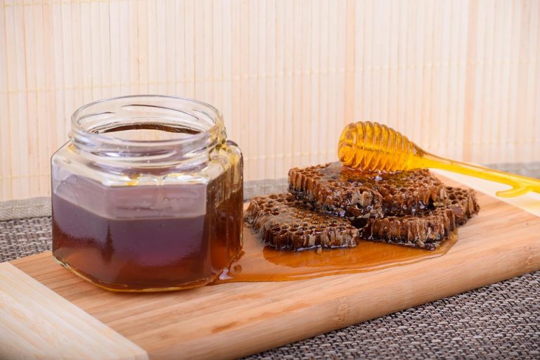 Honey jar and honeycomb on wooden board with dipper.