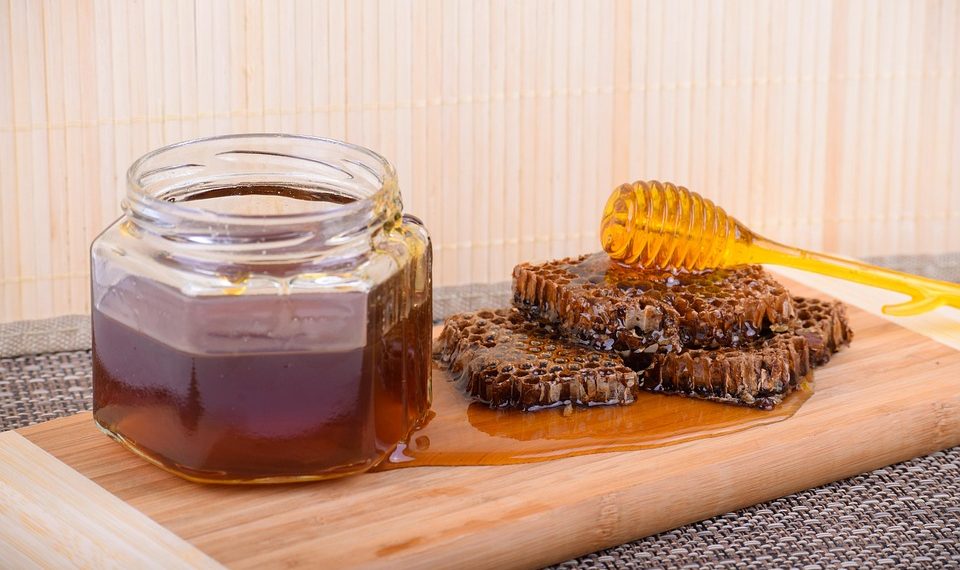 Honey jar and honeycomb on wooden board with dipper.