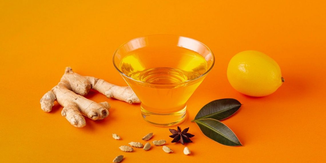 Ginger tea ingredients with ginger root, lemon, and spices on orange background.