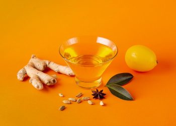 Ginger tea ingredients with ginger root, lemon, and spices on orange background.