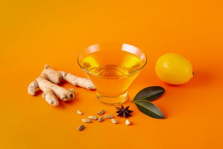 Ginger tea ingredients with ginger root, lemon, and spices on orange background.
