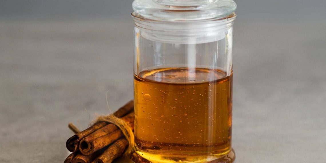 Cinnamon sticks and honey in a glass jar on gray background.