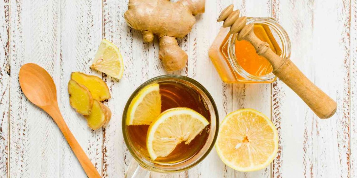 Ginger lemon tea with honey and fresh ginger slices on a wooden table.