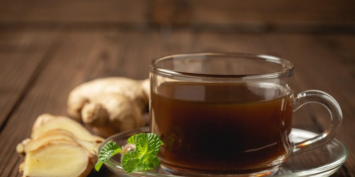 Steaming ginger tea with fresh ginger and mint leaves on wooden table.
