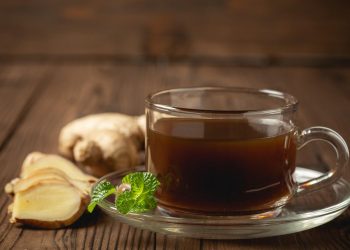 Steaming ginger tea with fresh ginger and mint leaves on wooden table.