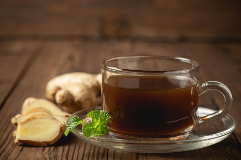 Steaming ginger tea with fresh ginger and mint leaves on wooden table.