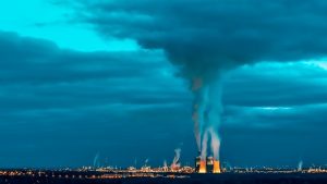 Power plant emitting smoke under cloudy sky with blue hues.