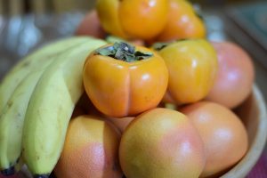 Bananas, persimmons, and grapefruits in a bowl.