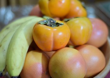Bananas, persimmons, and grapefruits in a bowl.