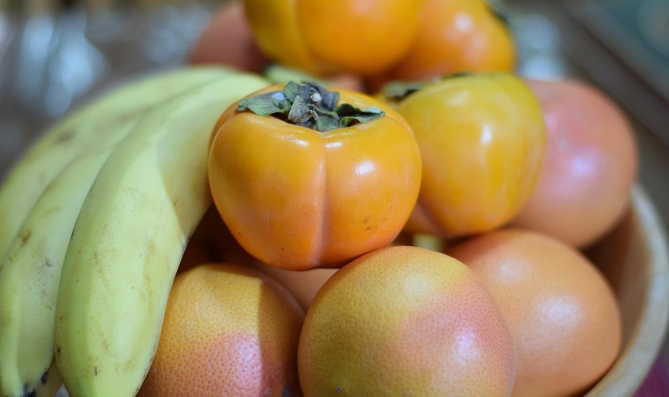 Bananas, persimmons, and grapefruits in a bowl.