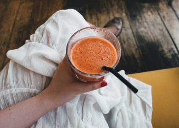 Hand holding a fresh orange smoothie with a straw.