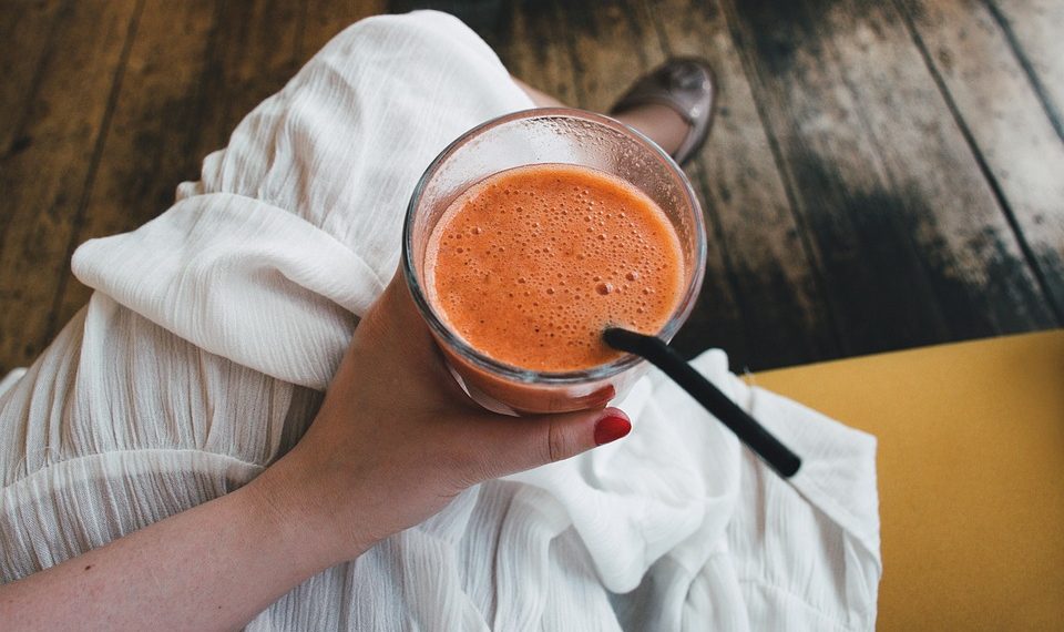 Hand holding a fresh orange smoothie with a straw.