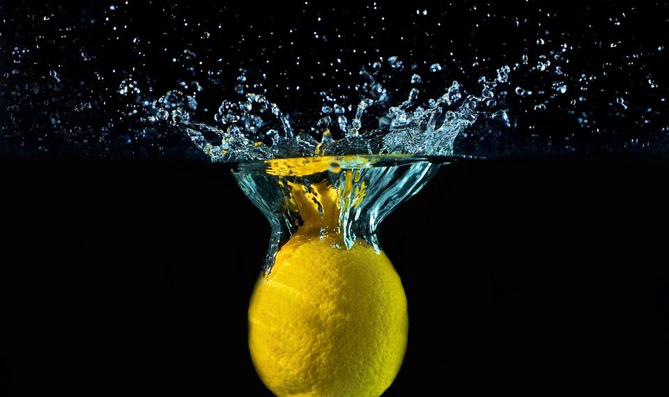 Lemon splashing into water creating ripples and bubbles.