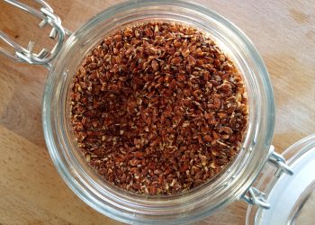 Jar filled with brown flaxseeds on wooden table top.