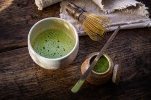 Green matcha tea with a bamboo whisk and powder on a rustic table.