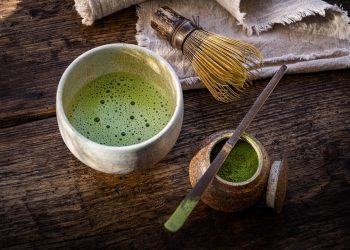 Green matcha tea with a bamboo whisk and powder on a rustic table.