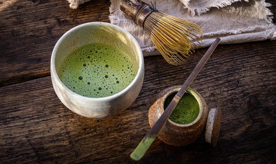 Green matcha tea with a bamboo whisk and powder on a rustic table.