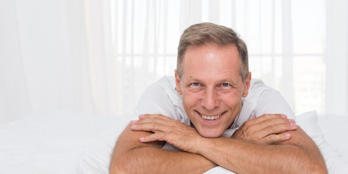Smiling man relaxing on bed in bright room.
