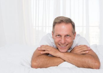 Smiling man relaxing on bed in bright room.