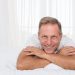 Smiling man relaxing on bed in bright room.