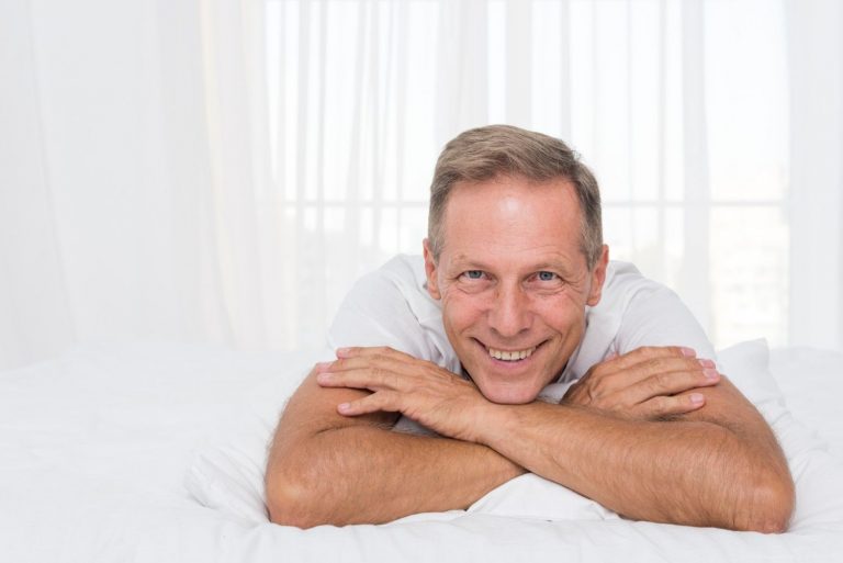 Smiling man relaxing on bed in bright room.