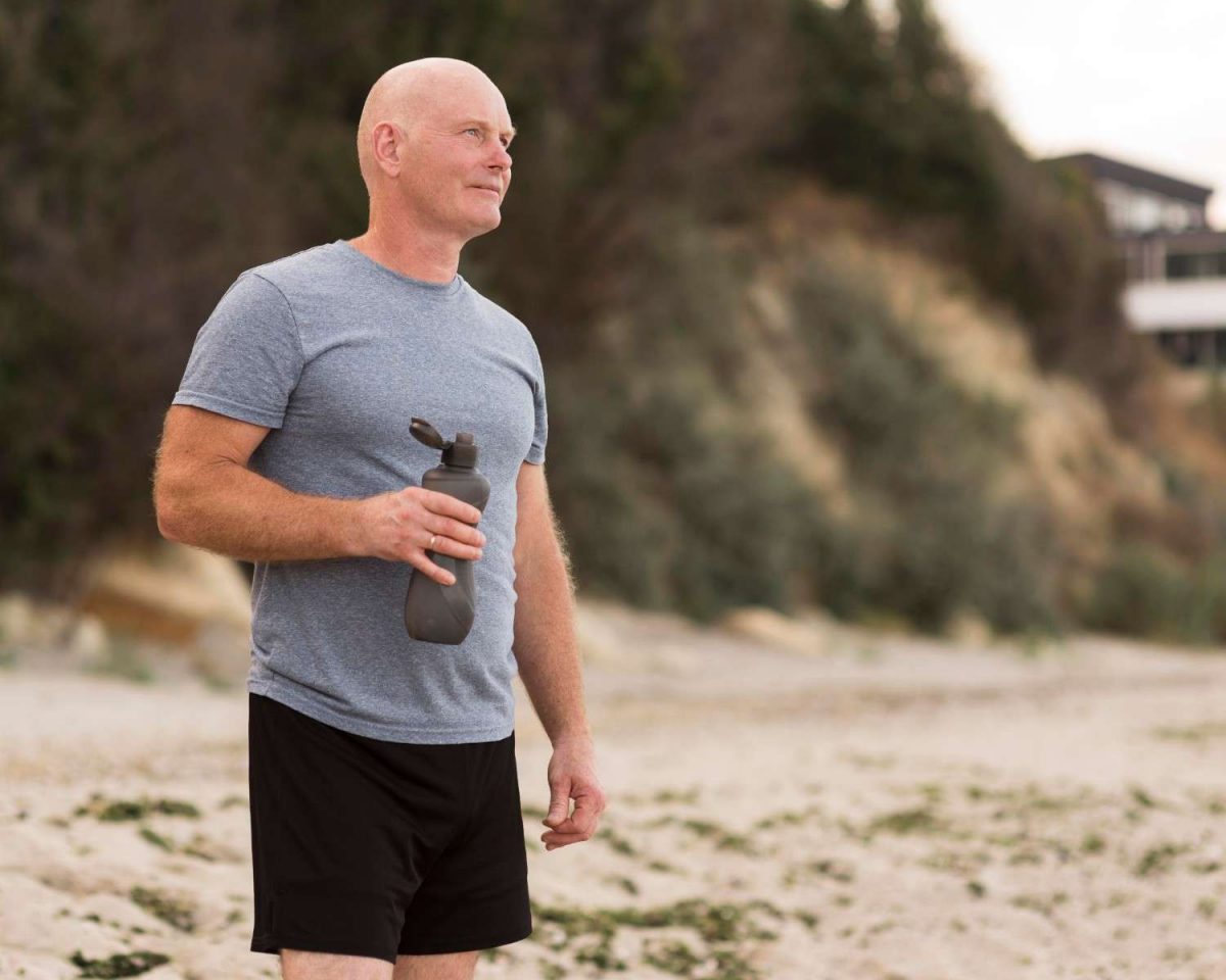 Man holding water bottle on the beach in athletic attire.
