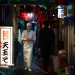 Chef walks through narrow Tokyo alleyway illuminated by lanterns.
