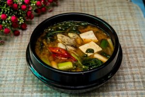 Korean tofu soup with vegetables in a black bowl.