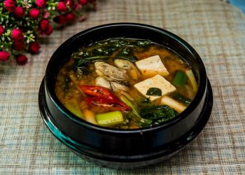 Korean tofu soup with vegetables in a black bowl.