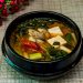 Korean tofu soup with vegetables in a black bowl.