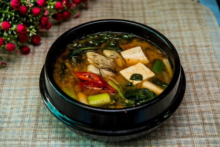 Korean tofu soup with vegetables in a black bowl.