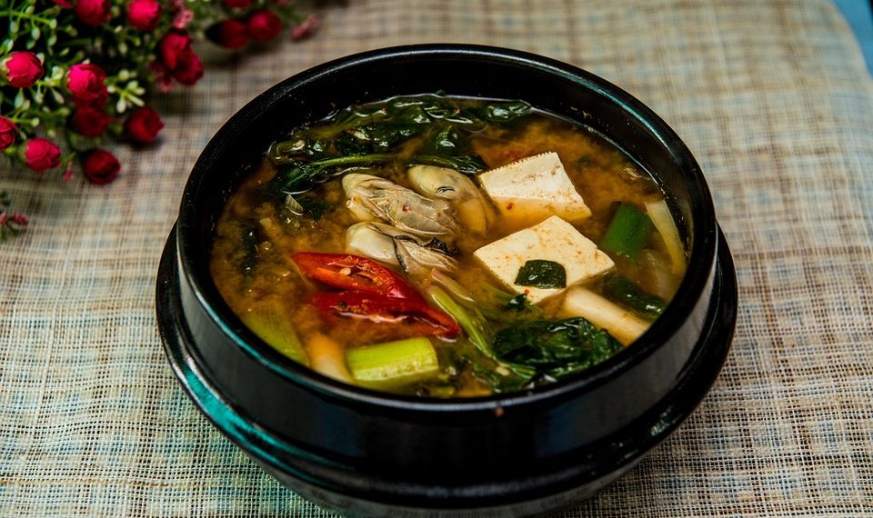 Korean tofu soup with vegetables in a black bowl.