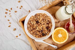 Bowl of granola with milk, orange, and honey on a wooden tray.