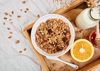 Bowl of granola with milk, orange, and honey on a wooden tray.
